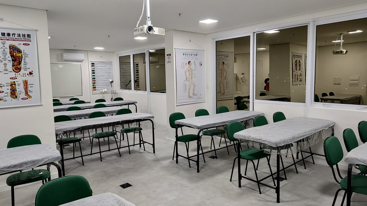 Sala de aula ampla e iluminada do Instituto Long Tao, com mesas de prática e mapas de acupuntura